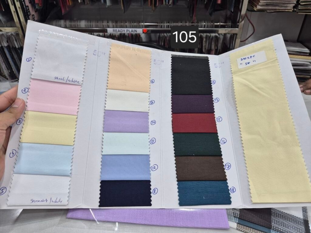 Open fabric swatch book showing rows of plain shirting colours and a pale yellow fabric sample.