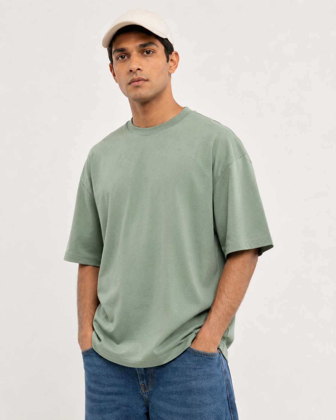 Model wearing a sage green oversized crew-neck T-shirt with dropped shoulders and blue jeans.